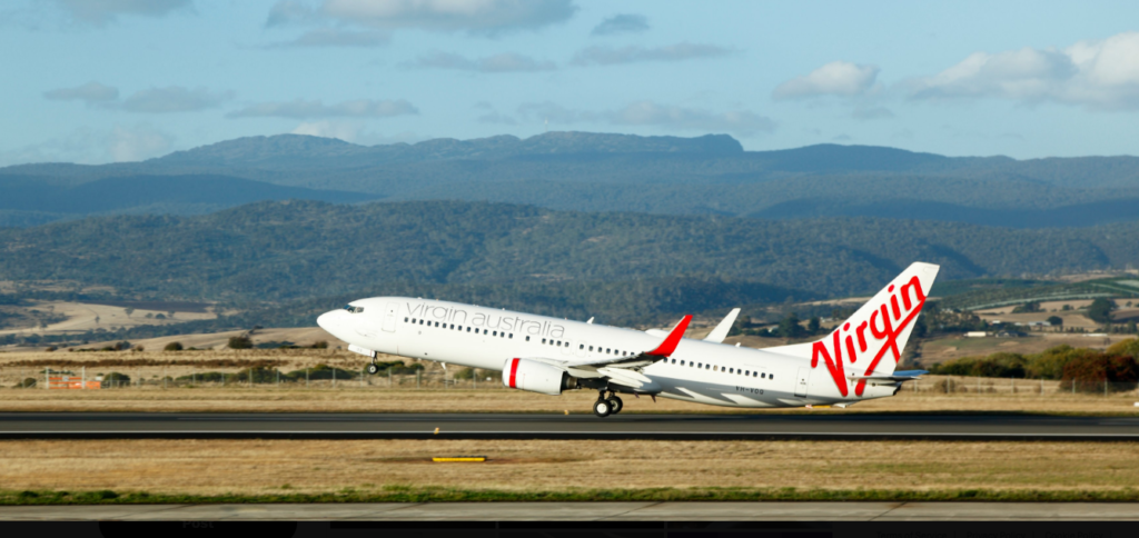 Sydney, Australia: Australia’s domestic aviation sector is struggling to match seat supply with surging passenger demand, with the Australian Competition and Consumer Commission (ACCC) warning that capacity remains below pre-pandemic levels despite a full recovery in travel volumes. According to the ACCC’s Domestic Airline Competition in Australia report released in August 2025, seat capacity in June was 2.8% lower than in June 2019, even though passenger numbers had fully recovered and, in some cases, exceeded pre-COVID benchmarks. In May 2025, Australian carriers transported 5.20 million domestic passengers, up 1.6% compared with May 2019. The mismatch between supply and demand is evident in the load factor, the proportion of available seats actually sold which rose to 80.7% in June 2025 from pre-pandemic averages of about 78%. The ACCC noted that the capacity shortfall has kept airfares elevated. Although jet fuel prices dropped by 12.3% year-on-year, average fares in June 2025 were still higher than the same month last year. The regulator attributed this to limited seating availability, which has reduced the scope for last-minute fare discounts, particularly on peak routes. “The lack of significant competition and constrained supply means consumers are seeing fewer low-fare options,” the ACCC said in its report. The sector has shown notable improvements in operational reliability. April 2025 recorded an on-time arrival rate of 82.4%, the highest in three years and above the long-term average of 80.7%. Cancellations have also remained low, averaging under 2.2% in April and May, with a slight uptick to 2.4% in June. Jetstar and Virgin Australia achieved the best punctuality and cancellation performance, while Qantas reported comparatively higher cancellation rates. The capacity lag stems from a combination of structural and market factors. The collapse of Tigerair in 2020 removed a substantial share of low-cost capacity from the market. New entrants such as Bonza have struggled to establish sustainable operations, and Rex’s expansion on trunk routes has been limited. Global supply chain disruptions and manufacturing delays have also constrained fleet expansion. Aircraft delivery backlogs, driven by production issues at major manufacturers, have delayed capacity growth plans for both Qantas and Virgin Australia. Qantas Group is in the process of receiving additional aircraft, including narrowbody jets redeployed from Jetstar Asia. Virgin Australia expects delivery of six Boeing 737 MAX 8 aircraft by December 2025. However, much of the incoming fleet will replace older planes rather than significantly expand seating capacity. Industry analysts note that upcoming infrastructure developments could provide relief. Slot reforms at congested airports and the opening of Western Sydney International (Nancy-Bird Walton) Airport in 2026 are expected to improve access for both existing and new operators. The ACCC has repeatedly expressed concern over the high level of market concentration, with Qantas Group and Virgin Australia controlling more than 98% of the domestic market (The Australian, Aug. 12, 2025). The regulator has urged measures to encourage competition, warning that the duopoly limits consumer choice and pricing flexibility. While passenger demand has fully recovered from pandemic lows, Australia’s domestic aviation market continues to operate with constrained capacity. The ACCC expects gradual improvement as airlines take delivery of new aircraft and as infrastructure projects come online, but warns that pricing pressure may persist in the near term.