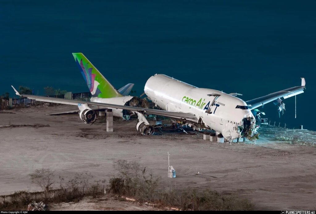 Hong Kong, China: Hong Kong’s Air Accident Investigation Authority (AAIA) has released its preliminary findings into last month’s fatal runway excursion involving an Emirates SkyCargo Boeing 747-481BDSF, operated by ACT Airlines, which veered off Runway 07L and plunged into the sea at Hong Kong International Airport on 20 October. The newly published report provides the first detailed account of the aircraft’s final moments but stops short of assigning cause, in line with international aviation investigation standards.
According to the AAIA, the freighter, operating as flight UAE9788 from Dubai World Central, completed a routine approach to Runway 07L shortly before 4 a.m. local time. The co-pilot had control of the aircraft during the landing, while the captain served as pilot monitoring. Weather conditions at the time were favourable, with visibility exceeding 10 kilometres and all navigation, communication, and surveillance systems functioning normally. No foreign object debris or airfield irregularities were reported prior to the landing.
After touchdown, the aircraft began decelerating as expected until an “AUTOBRAKES” alert appeared on the Engine Indication and Crew Alerting System. In response, the captain immediately took control of the aircraft. Within moments, the 747 began an uncommanded drift to the left and subsequently departed the runway surface abeam Taxiway C6. The aircraft broke through the airfield perimeter fence and collided with a stationary airport security vehicle positioned on the service road outside the runway boundary.
The force of the impact pushed the patrol vehicle into the sea, killing both security personnel inside. The 747 continued forward and came to rest partially submerged in the waters adjacent to the airport. Its tail section had separated during the violent sequence, and the aircraft was declared destroyed. All four crew members survived without injury.
The preliminary report reveals critical details from the flight data recorder that may help explain the aircraft’s sudden loss of directional control. Investigators confirmed that the aircraft had been dispatched under the Minimum Equipment List with the No. 4 engine thrust reverser inoperative, a condition permissible under the operator’s regulatory framework. While engines No. 2 and 3 entered reverse thrust at approximately 95% N1 and engine No. 1 entered idle reverse, engine No. 4 behaved abnormally. Instead of providing reverse or idle thrust, the outboard right engine began accelerating rapidly in the forward direction, reaching 90% N1 shortly after touchdown. Within seconds, it surged even further, climbing to more than 106% N1 before the aircraft left the runway. The strong forward thrust from a single engine created a severe asymmetry during the critical landing roll.
When investigators examined the flight deck after the accident, they found the thrust levers for engines 1, 2, and 3 fully closed with their reverse levers deployed to maximum. However, the No. 4 engine thrust lever was discovered in the full forward position, with its reverse lever also fully forward an unusual configuration that will be a major focus of the ongoing inquiry. The speed brake lever was in the flight detent position, and the autobrake selector had disarmed during the landing roll.
The AAIA has already completed extensive work, including securing and analysing the wreckage, retrieving the flight recorders, reviewing air traffic control surveillance data, studying foreign object debris detection reports, and interviewing both the flight crew and duty controllers. The investigation is now concentrating on several areas: the technical behaviour of the aircraft’s systems and engines at the time of the accident, the source and implications of the forward movement of the No. 4 thrust lever, the performance of the aircraft’s braking and thrust-reversing systems, and potential human factors. Investigators are also reviewing maintenance records, operational procedures, and the airline’s safety management practices.
The AAIA emphasised that the objective of the investigation is to prevent future accidents and not to apportion blame. A final report addressing the causes and contributing factors will be issued once the analysis is complete, a process that could take up to a year.