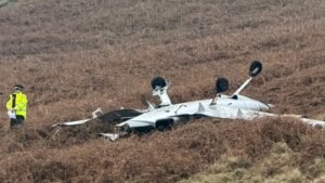 Littleborough, United Kingdom: Two men have died after a private light aircraft crashed in farmland near Littleborough, in the Rochdale district of Greater Manchester, police confirmed on Tuesday. Greater Manchester Police (GMP) said emergency services were called to reports of the incident shortly after 11 a.m. GMT on 3 February 2026. The crash occurred in a rural area close to Hollingworth Lake and Blackstone Edge, not far from the M62 motorway. Officers and paramedics quickly arrived on scene, supported by fire crews and specialist investigators from the Air Accidents Investigation Branch (AAIB). GMP confirmed the bodies of two men were found at the site and were pronounced dead by emergency responders. Preliminary data from flight-tracking services indicate the aircraft involved was a Cirrus SR20, a single-engine four-seat light aircraft commonly used in private and general aviation. The plane had reportedly departed Birmingham Airport’s XLR Executive Jet Centre at around 10 a.m. on Tuesday. It was tracked flying for approximately 40 minutes before its transponder signal stopped south of the M62 near Marsden, West Yorkshire, shortly before the crash. There were no other passengers on board, and there have been no confirmed injuries on the ground. Police established a secure perimeter around the crash site while emergency personnel conducted searches and evidence recovery. Road closures were in place in the immediate vicinity, and residents and visitors were asked to avoid the area to allow investigative work to continue. Images circulating on social media and confirmed by official statements show a yellow parachute canopy entangled on an electricity pylon near the scene. The Cirrus aircraft type involved is fitted with a Ballistic Recovery System (BRS), designed to deploy a whole-aircraft parachute in emergencies. At this stage, investigators have not provided a definitive explanation of whether the parachute was deliberately deployed by the pilot or triggered by impact forces. A National Grid spokesman said its engineers were on site supporting the emergency services, and there was no disruption to the local power supply. Chief Superintendent Danny Inglis, district commander for GMP’s Rochdale division, described the incident as “a devastating incident where two people have lost their lives,” and extended condolences to the families and friends of the deceased. He added that officers would remain at the scene into the following days to support investigators and collect evidence. The AAIB confirmed that it has launched a formal investigation into the accident and has deployed a multidisciplinary team of inspectors to examine wreckage, flight data, and other relevant materials. The regulatory body typically issues a preliminary report in the weeks following an accident and a full report in due course, depending on the complexity of the findings.