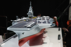 Macron Unveils ‘France Libre’ New Next-Gen Nuclear Aircraft Carrier Plan For France SEO DES: Designed as Europe’s largest warship, France Libre will be about 310m long with a displacement of 75,000–80,000 tonnes, boosting major naval capability SOCIAL: French President Emmanuel Macron has named France’s next-generation nuclear aircraft carrier “France Libre”, replacing the Charles de Gaulle by 2038 and boosting strategic autonomy. The €10 billion project, formerly PANG, will be Europe’s largest warship, powered by nuclear reactors and capable of operating Rafale jets, Hawkeye aircraft, and drones. Positioned as key to France’s defence strategy, the carrier boosts nuclear deterrence and expands global deployment capability amid rising geopolitical tensions. Paris, France: French President Emmanuel Macron has officially named France’s next-generation nuclear-powered aircraft carrier “France Libre”, marking a significant step in the country’s long-term naval modernization strategy and its push for strategic autonomy. Macron announced the name during a visit to the shipyard at Indret in western France, where early work on the vessel’s nuclear reactors has already begun. The name “France Libre” meaning “Free France”pays tribute to the World War II resistance movement led by Charles de Gaulle, symbolizing national resilience and independence. The new aircraft carrier will replace the aging Charles de Gaulle, currently France’s only aircraft carrier and the only nuclear-powered carrier in service outside the United States. Commissioned in 2001, the vessel is expected to retire by 2038, when the new carrier becomes operational following sea trials planned around 2036. The France Libre programme, previously known as the Porte-avions de nouvelle génération (PANG), forms the backbone of France’s future naval aviation capability. Designed to be the largest warship ever built in Europe, the France Libre will measure approximately 310 meters in length and displace around 75,000 to 80,000 tonnes. The carrier will be powered by two nuclear reactors, enabling extended deployment without frequent refuelling and reinforcing France’s nuclear deterrence posture. It is expected to carry: Around 30 Rafale fighter jets Airborne early warning aircraft such as E-2D Hawkeye Helicopters and next-generation unmanned aerial systems (UAVs/UCAVs) The vessel will also incorporate advanced launch and recovery systems, including electromagnetic catapults (EMALS), aligning it with next-generation carrier technologies. The programme is estimated to cost €10–10.2 billion ($11–12 billion), making it one of Europe’s most ambitious defence projects. Reactor component manufacturing began in 2025 Full-scale construction is expected around 2030–2031 Sea trials are projected for 2035–2036 Entry into service is targeted for 2038 The project involves major French defence and industrial players, including Naval Group, Chantiers de l’Atlantique, and TechnicAtome. Macron framed the programme as essential in an evolving global security environment, describing oceans as “new arenas of contemporary conflict.” France remains the only nuclear-armed nation in the European Union, and the new carrier will reinforce its ability to deploy nuclear-capable aircraft at sea. The announcement also comes amid heightened military activity, with France recently deploying the Charles de Gaulle and additional naval assets to the Mediterranean and Middle East in response to regional tensions. Paris views the programme as central to: Maintaining continuous carrier availability Strengthening NATO contributions while enhancing European defence autonomy Expanding global power projection, particularly in strategic maritime regions Beyond its military role, the name “France Libre” carries strong political symbolism. Macron described it as a commitment to national strength and independence, invoking the legacy of resistance and sovereignty. “In this name lives the memory to remain free, we must be powerful,” he said, linking historical identity with future defence ambitions. As Europe navigates an increasingly complex security landscape, the project signals France’s intent to combine historical legacy, nuclear capability, and advanced technology into a single strategic platform.