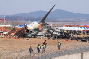 Jeju Air Crash Probe Finds Airport Structure May Have Worsened Deadly 2024 Disaster SEO DES: Investigators say the structure failed international standards requiring frangible supports, suggesting the crash might have been survivable otherwise SOCIAL: Investigations into the December 2024 crash of Jeju Air Flight 2216 at Muan International Airport, South Korea, have linked the disaster to longstanding airport infrastructure safety failures. The Boeing 737-800 belly-landed after a suspected bird strike but overran the runway and struck a rigid concrete embankment supporting a navigation localiser antenna, causing a catastrophic fire that killed 179 of the 181 people on board. Investigators say the structure did not meet international safety standards requiring frangible supports that break on impact, suggesting the crash may have been survivable otherwise. South Korea’s government has acknowledged the safety lapse, launched an independent inquiry, and begun reviewing runway infrastructure nationwide while a final investigation report is expected in 2026. Image: Aero Time Video: TOI Muan, South Korea: Investigations into the 2024 crash of a Jeju Air passenger jet in South Korea have revealed that longstanding airport infrastructure failures likely played a critical role in turning a survivable emergency landing into the country’s deadliest aviation disaster. Jeju Air Flight 2216, a Boeing 737-800 operating from Bangkok to Muan, crashed at Muan International Airport on 29 December 2024, killing 179 of the 181 people on board. Only two cabin crew members survived the accident. Recent findings cited in a government-commissioned report suggest that the aircraft’s occupants may have survived if the plane had not collided with a rigid concrete structure located at the end of the runway. The aircraft had belly-landed during an emergency approach and slid beyond the runway before striking a concrete mound supporting a navigation localiser antenna, triggering a catastrophic fire. The concrete embankment that the aircraft struck has become a central focus of the investigation. Structural simulations conducted after the accident indicated that the impact with the runway overrun itself was survivable and that the aircraft could have come to a halt with far fewer casualties if the structure had been designed to break on impact. Experts and lawmakers have argued that the structure did not meet international aviation safety standards, which typically require runway navigation equipment to be mounted on “frangible” supports designed to collapse during an aircraft collision. South Korea’s transport authorities later acknowledged that the embankment contributed to the severity of the crash and announced plans to remove or redesign similar structures at several airports across the country. Opposition lawmakers have also blamed decades of government negligence, noting that the problematic structure had existed since the late 1990s without corrective action despite safety concerns. Investigators believe the emergency landing was triggered by a bird strike during the aircraft’s final approach. Remains of birds were found in both engines during the preliminary investigation. Evidence later indicated that the pilots may have inadvertently shut down the less-damaged engine after the bird strike, potentially reducing available thrust during the emergency landing attempt. The aircraft ultimately landed without deploying its landing gear and slid along the runway before colliding with the concrete structure at the runway’s end, leading to an explosion and fire that destroyed the aircraft. The disaster has triggered widespread criticism of the investigation process and government oversight of aviation safety. Families of the victims have accused authorities of delaying reports and failing to provide transparency about the causes of the crash. In response to mounting pressure, South Korea’s parliament approved an independent inquiry to examine the accident, including the role of bird strikes, possible mechanical failures, and the runway structure that the aircraft struck. South Korea’s Transport Ministry has also acknowledged that a navigation structure at Muan International Airport failed to meet safety standards, contributing to the deadly crash of a Jeju Air Boeing 737-800 in December 2024. Authorities admitted the structure should have been designed to break on impact, in line with international safety guidelines, and its rigid construction likely worsened the disaster. A final report from investigators is expected in 2026, as officials continue to analyze flight data, cockpit recordings and infrastructure safety standards. The tragedy remains the deadliest aviation accident in South Korean history and has prompted a nationwide review of runway safety areas and navigation equipment installations at airports across the country.