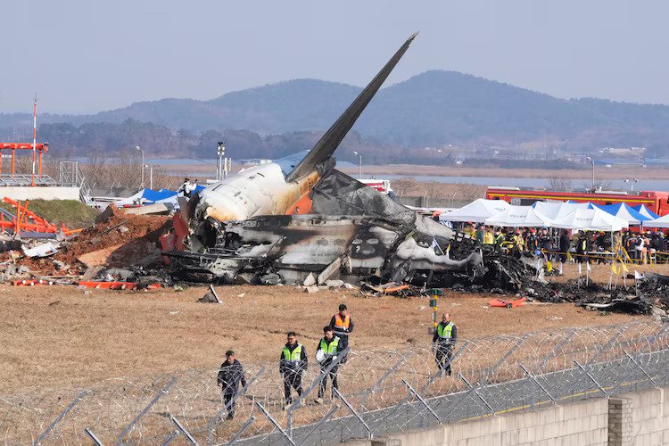 Jeju Air Crash Probe Finds Airport Structure May Have Worsened Deadly 2024 Disaster SEO DES: Investigators say the structure failed international standards requiring frangible supports, suggesting the crash might have been survivable otherwise SOCIAL: Investigations into the December 2024 crash of Jeju Air Flight 2216 at Muan International Airport, South Korea, have linked the disaster to longstanding airport infrastructure safety failures. The Boeing 737-800 belly-landed after a suspected bird strike but overran the runway and struck a rigid concrete embankment supporting a navigation localiser antenna, causing a catastrophic fire that killed 179 of the 181 people on board. Investigators say the structure did not meet international safety standards requiring frangible supports that break on impact, suggesting the crash may have been survivable otherwise. South Korea’s government has acknowledged the safety lapse, launched an independent inquiry, and begun reviewing runway infrastructure nationwide while a final investigation report is expected in 2026. Image: Aero Time Video: TOI Muan, South Korea: Investigations into the 2024 crash of a Jeju Air passenger jet in South Korea have revealed that longstanding airport infrastructure failures likely played a critical role in turning a survivable emergency landing into the country’s deadliest aviation disaster. Jeju Air Flight 2216, a Boeing 737-800 operating from Bangkok to Muan, crashed at Muan International Airport on 29 December 2024, killing 179 of the 181 people on board. Only two cabin crew members survived the accident. Recent findings cited in a government-commissioned report suggest that the aircraft’s occupants may have survived if the plane had not collided with a rigid concrete structure located at the end of the runway. The aircraft had belly-landed during an emergency approach and slid beyond the runway before striking a concrete mound supporting a navigation localiser antenna, triggering a catastrophic fire. The concrete embankment that the aircraft struck has become a central focus of the investigation. Structural simulations conducted after the accident indicated that the impact with the runway overrun itself was survivable and that the aircraft could have come to a halt with far fewer casualties if the structure had been designed to break on impact. Experts and lawmakers have argued that the structure did not meet international aviation safety standards, which typically require runway navigation equipment to be mounted on “frangible” supports designed to collapse during an aircraft collision. South Korea’s transport authorities later acknowledged that the embankment contributed to the severity of the crash and announced plans to remove or redesign similar structures at several airports across the country. Opposition lawmakers have also blamed decades of government negligence, noting that the problematic structure had existed since the late 1990s without corrective action despite safety concerns. Investigators believe the emergency landing was triggered by a bird strike during the aircraft’s final approach. Remains of birds were found in both engines during the preliminary investigation. Evidence later indicated that the pilots may have inadvertently shut down the less-damaged engine after the bird strike, potentially reducing available thrust during the emergency landing attempt. The aircraft ultimately landed without deploying its landing gear and slid along the runway before colliding with the concrete structure at the runway’s end, leading to an explosion and fire that destroyed the aircraft. The disaster has triggered widespread criticism of the investigation process and government oversight of aviation safety. Families of the victims have accused authorities of delaying reports and failing to provide transparency about the causes of the crash. In response to mounting pressure, South Korea’s parliament approved an independent inquiry to examine the accident, including the role of bird strikes, possible mechanical failures, and the runway structure that the aircraft struck. South Korea’s Transport Ministry has also acknowledged that a navigation structure at Muan International Airport failed to meet safety standards, contributing to the deadly crash of a Jeju Air Boeing 737-800 in December 2024. Authorities admitted the structure should have been designed to break on impact, in line with international safety guidelines, and its rigid construction likely worsened the disaster. A final report from investigators is expected in 2026, as officials continue to analyze flight data, cockpit recordings and infrastructure safety standards. The tragedy remains the deadliest aviation accident in South Korean history and has prompted a nationwide review of runway safety areas and navigation equipment installations at airports across the country.