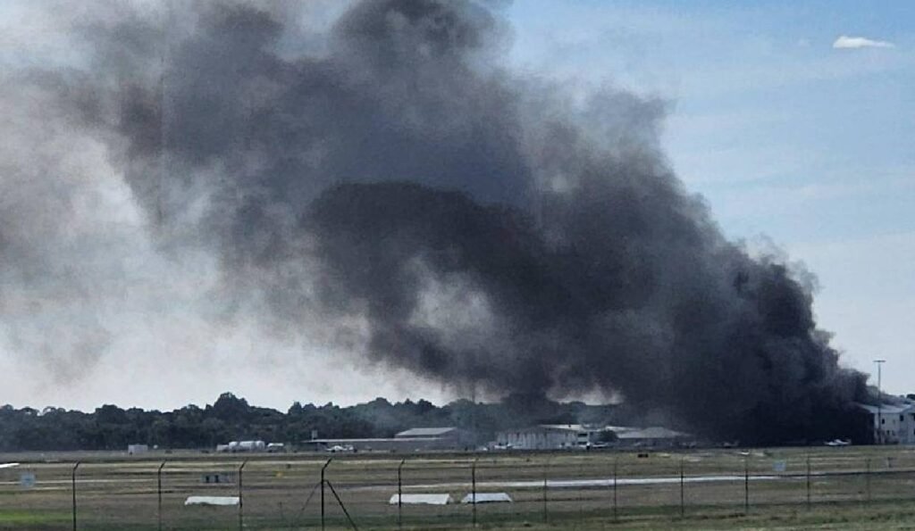 Adelaide, Australia: A light aircraft crash at Parafield Airport on Wednesday afternoon has left two people dead and at least 11 others injured after the plane slammed into a hangar and triggered a major fire, authorities confirmed. The aircraft, identified as a Diamond DA42 twin-engine training plane, was carrying two occupants, a pilot and one passenger both of whom were killed in the crash. Officials have yet to release their identities. No other passengers were onboard, confirming the total number of people in the aircraft at the time was two. The incident occurred at approximately 2:10 pm local time as the aircraft was attempting to land. During the approach, the plane reportedly lost control and crashed into a hangar, believed to be Hangar 54, causing a powerful impact that ignited aviation fuel and set off a large blaze. Thick black smoke was seen billowing into the sky as emergency services rushed to the scene. The crash resulted in significant injuries on the ground. At least 11 people inside the hangar were injured, with emergency officials confirming that one person suffered life-threatening burns and two others sustained serious injuries, while several others were treated for minor injuries and smoke inhalation. The injured were transported to nearby hospitals, including Royal Adelaide Hospital and Lyell McEwin Hospital. Firefighters and emergency responders acted swiftly to contain the blaze, deploying multiple crews to bring the fire under control despite challenging conditions. Authorities evacuated nearby areas and issued public safety alerts due to heavy smoke. The airport was temporarily closed to all air traffic as emergency operations and safety inspections were carried out. The Australian Transport Safety Bureau (ATSB) has launched a formal investigation into the accident. Investigators will examine the wreckage, flight conditions and any potential technical or operational factors that may have contributed to the crash. Preliminary witnesses suggest the aircraft may have experienced difficulty shortly before impact, though officials have not confirmed a cause. Parafield Airport is located about 18 kilometres north of Adelaide, is one of Australia’s busiest general aviation and pilot training hubs, frequently used by flight schools.
