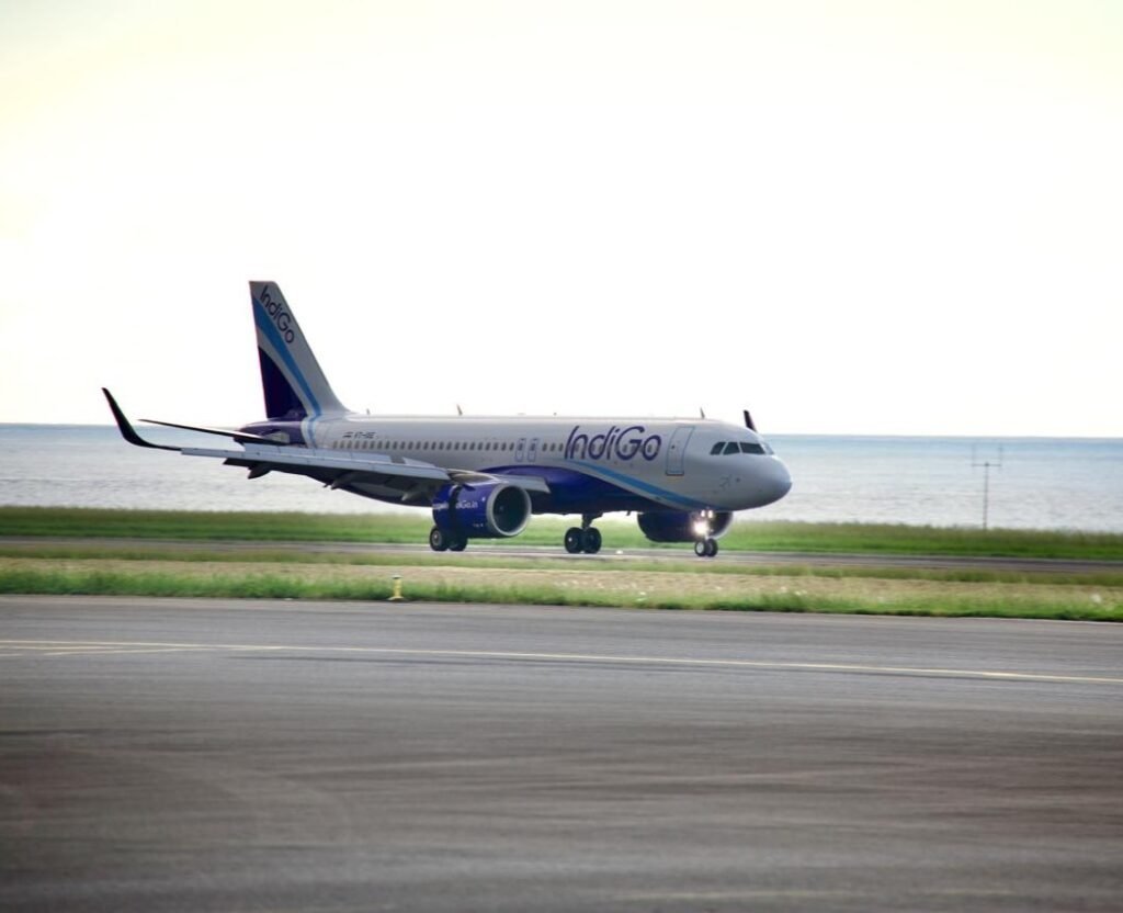 New Delhi, India: InterGlobe Aviation, the parent company of India’s largest airline, IndiGo, reported a consolidated net loss of ₹2,536.9 crore for the quarter ended March 31, 2026 (Q4 FY26), reversing from a net profit of ₹3,067.5 crore recorded during the corresponding quarter of the previous financial year. The sharp decline in profitability came amid significant foreign exchange losses, elevated fuel prices, operational disruptions, and one-time charges that weighed heavily on the carrier’s financial performance despite a marginal increase in revenue. According to the airline’s financial results, revenue from operations rose 1.3% year-on-year to ₹22,438 crore in the January-March 2026 quarter, compared with ₹22,152 crore in Q4 FY25. However, the increase in revenue was insufficient to offset mounting cost pressures. A major factor behind the quarterly loss was a foreign exchange loss of approximately ₹4,823 crore, driven by the depreciation of the Indian rupee against the US dollar. The impact was particularly significant for IndiGo as a large portion of its expenses including aircraft leases, maintenance costs and other aviation-related payments are dollar-denominated. The airline also faced rising aviation turbine fuel (ATF) costs during the quarter amid geopolitical tensions and higher crude oil prices. Fuel remains one of the largest expense components for airlines and contributed substantially to the pressure on margins. In addition, IndiGo reported a one-time charge of ₹250 crore during the quarter. The airline also continued to face operational challenges, including disruptions linked to airspace restrictions and capacity-related constraints that affected network efficiency. Despite the reported loss, the company stated that its underlying business performance remained profitable. Excluding the impact of foreign exchange fluctuations and exceptional items, IndiGo posted a net profit of approximately ₹1,921 crore during the quarter. For the full financial year ended March 31, 2026, IndiGo reported a consolidated net loss of around ₹2,394 crore. The company’s annual results were affected by foreign exchange losses of nearly ₹8,100 crore, disruption-related costs estimated at about ₹580 crore, and expenses of roughly ₹1,200 crore associated with the implementation of new labour regulations. At the operational level, IndiGo carried approximately 123.4 million passengers during FY26, representing a 4% increase compared with the previous year. Total income for the fiscal year rose 6.4% to ₹89,513 crore, reflecting continued demand growth in India’s aviation sector despite a challenging operating environment. The airline’s board also approved the partial prepayment of finance lease obligations owed to its wholly-owned subsidiary, InterGlobe Aviation Financial Services IFSC Private Limited. The prepayment, to be executed in one or more tranches, may total up to US$450 million and is intended to support future aircraft and aviation asset acquisitions. Management indicated that IndiGo is evaluating fuel hedging strategies after remaining largely unhedged during a period of heightened volatility in crude oil prices. The airline said such measures could help reduce exposure to future fuel price fluctuations. Looking ahead, IndiGo expects capacity growth to moderate in the near term. The airline has guided for capacity expansion of approximately 3-4% in the first quarter of FY27, significantly lower than the 16.4% growth recorded during the corresponding period a year earlier. Following the earnings announcement, market participants indicated that IndiGo shares would remain in focus as investors assess the impact of currency movements, fuel costs, regulatory developments and operational performance on the airline’s future profitability.