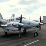 New Mexico, United States: The U.S. National Transportation Safety Board (NTSB) has revealed that a U.S. military GPS jamming exercise was underway when a Beechcraft C90 King Air air ambulance crashed into mountainous terrain near Lincoln, New Mexico, killing all four people on board. The findings were released in a preliminary report, meaning investigators have not yet determined the probable cause or contributing factors of the accident. The accident occurred at 0015 local time on May 14, 2026, after the aircraft, registered N249CP and operated by Generations Jets under Part 135 as an air ambulance flight, departed Roswell Air Center (ROW) to Sierra Blanca Regional Airport (SRR) in Ruidoso to pick up a patient for transport to Albuquerque. The flight was crewed by two pilots and carried two flight nurses employed by Trans Aero Medical Services. The crash claimed the lives of Captain Keelan Clark, First Officer Ali Kawsara, and flight nurses Sarah Clark and Jamie Novick. According to the NTSB, GPS jamming activities conducted by the U.S. military were active over the accident area during the flight. Shortly after departure, the aircraft was cleared to 12,000 feet under instrument flight rules (IFR). At 0000:26, air traffic controllers advised the crew that the aircraft had climbed to 13,000 feet, 1,000 feet above its assigned altitude. The pilot responded that the aircraft had lost GPS capability and requested headings from air traffic control. The crew initially requested the RNAV (GPS) Runway 24 approach into Sierra Blanca Regional Airport but, after losing GPS navigation, switched to the ILS Runway 24 approach. At 0001:17, the Albuquerque Air Route Traffic Control Center (ARTCC) controller contacted the operations supervisor and requested that the military stop the GPS jamming. The aircraft continued north while controllers provided radar headings. During the same period, three other aircraft also reported GPS outages, with one crew requiring additional assistance to identify a ground-based navigation aid. At about 0005, the ARTCC operations supervisor again contacted the military to stop the jamming, after which ADS-B transmissions returned to normal. At 0008, the accident crew reported having Ruidoso in sight and requested to continue visually. Controllers cleared the aircraft for a visual approach and advised the crew they could cancel IFR after descending below 9,000 feet or after landing. The pilots acknowledged the clearance and stated they would cancel IFR "in just a couple of minutes." No further radio transmissions were received. The aircraft then turned southwest toward Sierra Blanca Regional Airport. Between the airport and the aircraft lay the Capitan Mountains, which rise to 10,201 feet. Around 0010, after being informed the aircraft was on a visual approach, the military resumed the GPS jamming exercise. The King Air began descending before briefly climbing again. The final Spidertracks data point recorded the aircraft at 9,823 feet, 150 knots ground speed, and a heading of 250 degrees. Seconds later, it struck terrain at an elevation of about 9,950 feet, approximately 730 feet east and 230 feet below the Capitan Mountains Summit Radio Facility, triggering a post-impact fire that ignited a forest fire. Investigators also found that the crew's ForeFlight weather briefing included active NOTAMs warning that military GPS jamming would affect GPS, WAAS, GBAS and ADS-B navigation over a wide area encompassing the accident flight path and altitudes. Additional NOTAMs advised that Sierra Blanca Regional Airport's automated weather observation system (AWOS) was out of service, while the weather briefing indicated no METAR or TAF was available for the destination airport. The airport's published RNAV and ILS Runway 24 approach procedures also state that the procedures are not authorized when the local altimeter setting is unavailable. The NTSB emphasized that the report is preliminary and subject to change, and that it does not determine the accident's probable cause.