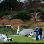 Carlisle, United States: A Cessna 150 collided with a Pennsylvania State Police Bell 407 helicopter at Carlisle Regional Airport in Cumberland County, Pennsylvania, on Wednesday evening, August 19, killing the Cessna pilot and injuring two state police troopers aboard the helicopter. The collision occurred near a runway at the airport, about 110 miles northwest of Philadelphia. The FAA identified the aircraft involved as a Cessna 150 and a Bell 407. The Cessna pilot, believed to have been the aircraft's only occupant, died in the crash. Authorities had not released the pilot's identity pending notification of next of kin. The Bell 407 was operated by the Pennsylvania State Police and was carrying two members of the department's aviation unit, Cpl. Bryce Corman and Tpr. Jason Mills. The helicopter was conducting a routine training exercise at Carlisle after operating from its Harrisburg base. According to Acting Pennsylvania State Police Commissioner Lt. Col. George Bivens, the helicopter was positioned several feet above a grassy area next to a runway when the Cessna approached from behind. The aircraft came down along the runway before veering sharply to the right at the last moment and striking the helicopter from the rear. “As that Cessna came down along that runway for an unknown reason, it veered hard to the right. At the last moment, it struck the helicopter from the rear,” Bivens said. The Cessna struck the helicopter's rear section, involving the tail rotor and then the main rotor, sending both aircraft into a violent crash. The Cessna broke into multiple pieces, while the Bell 407 lost its rotor blades and tail boom before rolling over and coming to rest on its side, partially on its roof. The two troopers were initially trapped inside the helicopter. Corman was able to push out a window and help Mills escape through the opening. Mills was believed to have suffered more serious injuries and significant bleeding, according to Bivens. Both troopers were taken to Penn State Health Milton S. Hershey Medical Center. Dr. Ashley Ludwig, the hospital's trauma medical director, said they arrived as Level 1 trauma patients but had only minor injuries and were in stable condition. One was expected to be discharged Wednesday night, while the other was admitted for further observation. Pennsylvania State Police Commissioner Col. Christopher Paris said the helicopter crew was conducting routine training when the collision occurred. He said the helicopter pilots would not have been able to see the Cessna approaching from behind. “The pilots would not have been able to even see that airplane approaching them,” Paris said. Governor Josh Shapiro visited the medical center and praised the emergency response and medical teams involved in treating the injured troopers. “Tonight could have been much worse,” Shapiro said, adding that the response was “an example of Pennsylvania at its finest.” Emergency personnel responded to the airport following the crash, and the coroner was called to the scene. Local residents Patrick Brown and Lloyd Slusser also reportedly crossed a fence and ran toward the wreckage to assist after witnessing the crash. The Cessna was reportedly from the local area, but authorities have not disclosed its departure point, destination or the purpose of its flight. The aircraft's pilot was believed to be its sole occupant. The exact cause of the collision remains undetermined. Officials said the Cessna's sudden right turn was made for an unknown reason, and investigators will examine why the aircraft veered from its approach path, the helicopter's position, airport operations and communications. Carlisle Regional Airport does not have an air traffic control tower. Pilots operating there use a common traffic radio frequency, and investigators are expected to examine those communications as part of the inquiry. State police also secured photographs and video that could assist investigators in reconstructing the collision. The FAA and National Transportation Safety Board are leading the investigation, with Pennsylvania State Police assisting. The NTSB said the wreckage would be documented and moved to a secure facility for further examination. Although the FAA and NTSB described the incident as a midair collision, Pennsylvania State Police later said the helicopter was on the ground at the time of the impact. Officials have not yet established whether the Cessna was airborne at the exact moment of contact. The distinction, along with the reason for the Cessna's sudden deviation, remains part of the investigation. No final cause has been determined, and authorities have not attributed the crash to pilot error, mechanical failure, communications issues or any other specific factor.